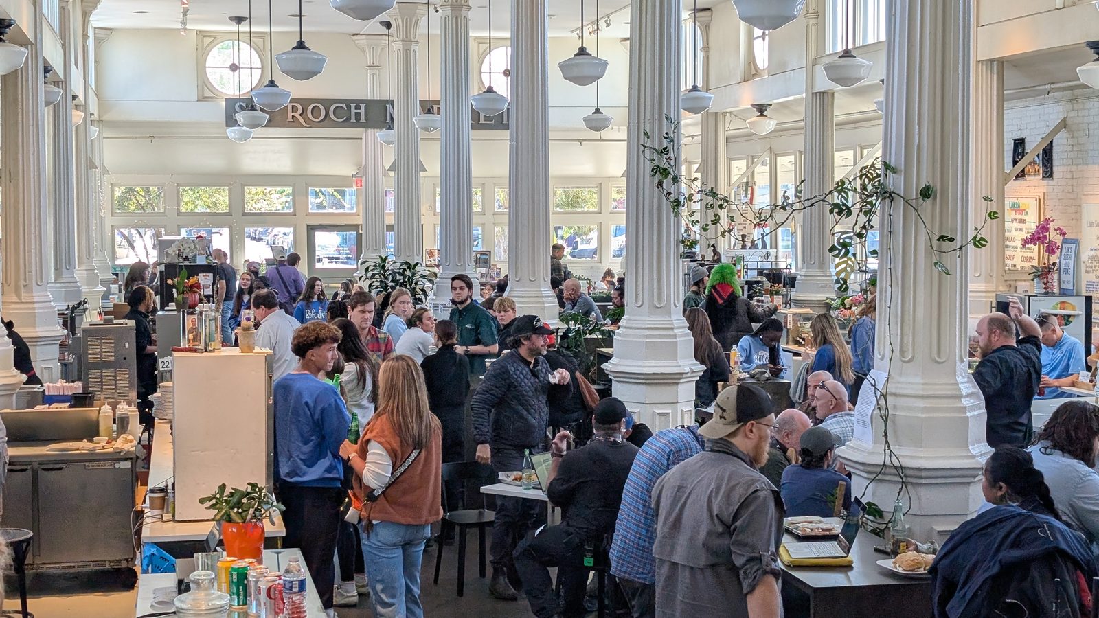 A busy evening inside St. Roch Market with guests gathered between the white cast iron columns